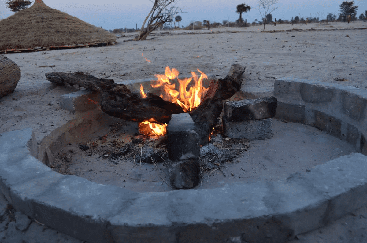 a fire pit in the sand with a hut in the background